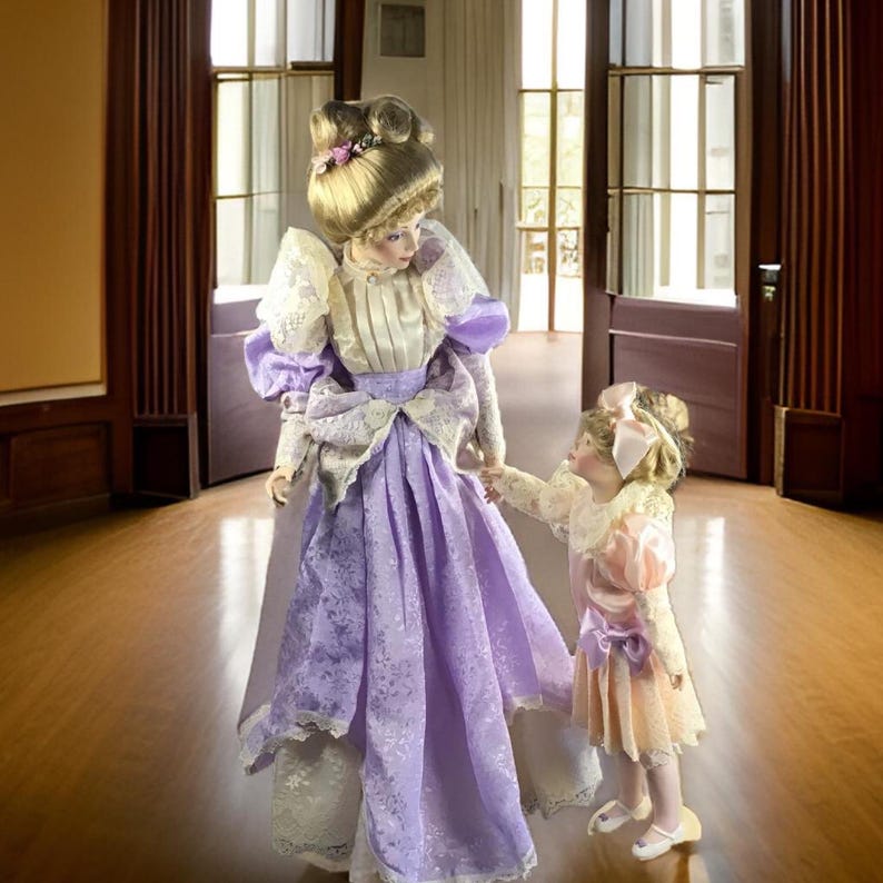 Puede incluir: Dos mu&ntilde;ecas de porcelana vestidas con ropa de estilo vintage. La mu&ntilde;eca m&aacute;s alta lleva un vestido lavanda con ribetes de encaje y un lazo blanco. La mu&ntilde;eca m&aacute;s baja lleva un vestido melocot&oacute;n con un lazo rosa y ribetes de encaje blanco. Ambas mu&ntilde;ecas tienen el pelo rubio y caras pintadas.