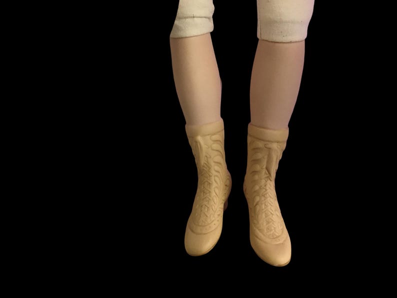 Puede incluir: Un par de botines beige de tobillo con detalles intrincados en la parte delantera. Las botas tienen la punta cerrada y un tac&oacute;n bajo.