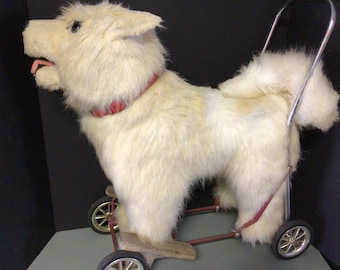 May include: A white plush dog on wheels. The dog is wearing a red collar and has a long, fluffy tail. The wheels are black with silver spokes.