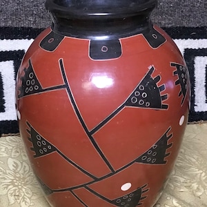 May include: A red ceramic vase with black and white geometric designs. The vase has a rounded body and a wide mouth.