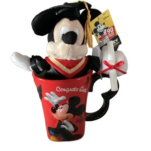 May include: A red ceramic mug with a black handle and a Mickey Mouse design. The mug says "Congrats Grad" and features a graduation cap. A plush Mickey Mouse wearing a graduation cap and gown is sitting inside the mug. A white graduation scroll with a red ribbon is attached to the mug.