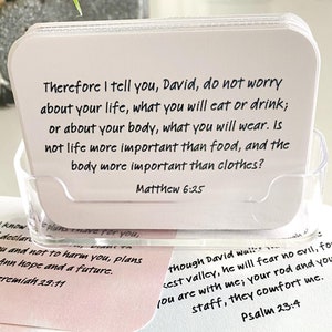 May include: A set of white cards with inspirational quotes from the Bible. The cards are in a clear acrylic holder. The text on the card reads: "Therefore I tell you, David, do not worry about your life, what you will eat or drink; or about your body, what you will wear. Is not life more important than food, and the body more important than clothes? Matthew 6:25"