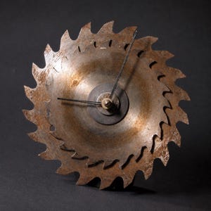 May include: A unique wall clock made from a circular saw blade. The clock features a rusty, aged appearance with black clock hands and a central mechanism. The saw blade's teeth are clearly visible, adding to its industrial aesthetic.