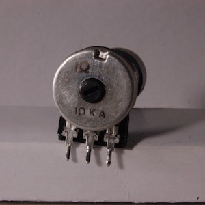 Peut inclure: Une tasse en c&eacute;ramique blanche avec une anse noire et l'inscription "But First, Coffee" en gras noir. La tasse est pos&eacute;e sur un fond flou, sugg&eacute;rant un cadre chaleureux.