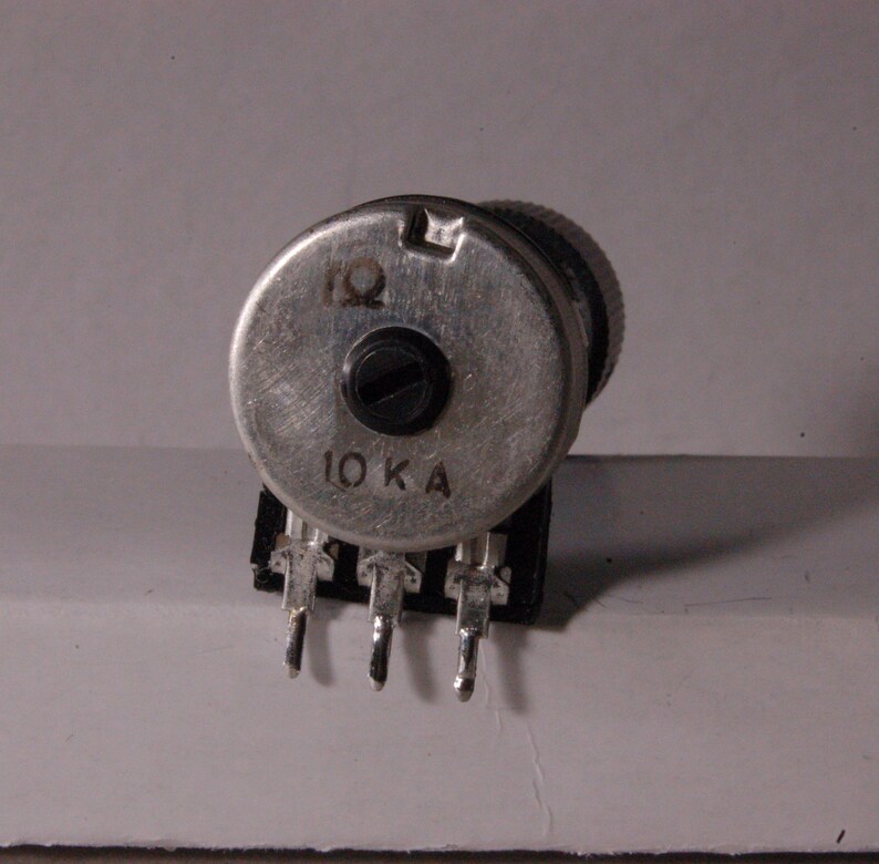 Peut inclure: Une tasse en c&eacute;ramique blanche avec une anse noire et l'inscription "But First, Coffee" en gras noir. La tasse est pos&eacute;e sur un fond flou, sugg&eacute;rant un cadre chaleureux.