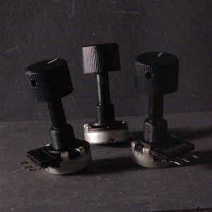 Peut inclure: Trois potentiom&egrave;tres noirs avec des boutons rainur&eacute;s et des marquages blancs. Les potentiom&egrave;tres ont une base cylindrique avec trois broches. Les boutons sont cylindriques avec un indicateur de ligne.