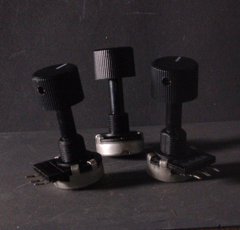 Peut inclure: Trois potentiom&egrave;tres noirs avec des boutons rainur&eacute;s et des marquages blancs. Les potentiom&egrave;tres ont une base cylindrique avec trois broches. Les boutons sont cylindriques avec un indicateur de ligne.