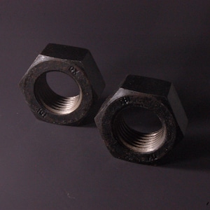 May include: Two dark gray, hexagonal nuts with threaded interior holes. The nuts have a metallic sheen and are set against a dark background. The image highlights the industrial design and construction of the nuts.