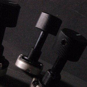 Peut inclure: Gros plan sur trois boutons de commande noirs avec des dessus stri&eacute;s et un petit indicateur de ligne blanche. Les boutons sont fix&eacute;s &agrave; des tiges noires avec des bases filet&eacute;es et des composants m&eacute;talliques argent&eacute;s. Le fond est sombre.