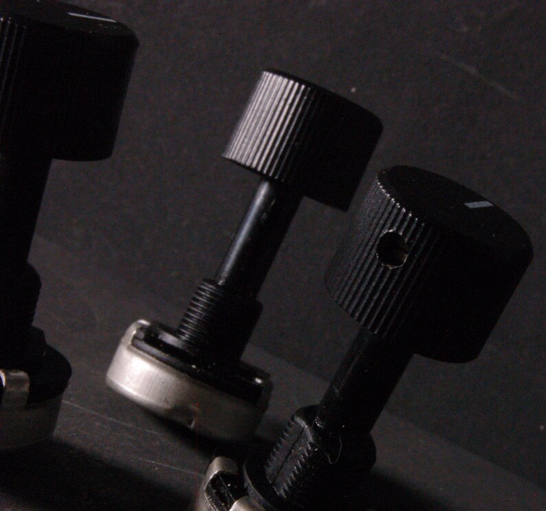 Peut inclure: Gros plan sur trois boutons de commande noirs avec des dessus stri&eacute;s et un petit indicateur de ligne blanche. Les boutons sont fix&eacute;s &agrave; des tiges noires avec des bases filet&eacute;es et des composants m&eacute;talliques argent&eacute;s. Le fond est sombre.