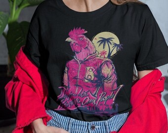 May include: A black t-shirt with a pink rooster wearing a pink jacket and a black letter "B" on the front. The rooster is standing in front of a sunset with palm trees. The text "Don't Like Other People?" is printed below the rooster.