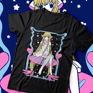 May include: Black t-shirt with a graphic of an anime character with long blonde hair sitting on a pink flying saucer. The character is wearing a white dress and has a pink heart on her chest. The text "なもり" is written in Japanese on the saucer.