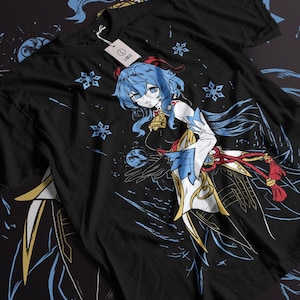 Peut inclure: T-shirt noir avec un motif de personnage d'anime bleu et blanc. Le personnage est une femme aux cheveux bleus et une tenue blanche et bleue. Elle tient un orbe bleu dans sa main. L'arri&egrave;re-plan est noir avec des flocons de neige.