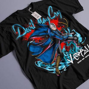 Peut inclure: T-shirt noir avec un motif bleu et rouge d'un personnage du jeu vidéo Devil May Cry. Le personnage tient une épée et porte une cape bleue. Le texte "Devil May Cry" est écrit en lettres bleues et rouges. Le texte "Vergil Son of Sparda" est écrit en lettres blanches.
