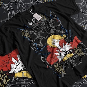 Peut inclure: T-shirt noir avec un imprimé graphique blanc de deux personnages d'anime. Le personnage de gauche porte un casque et une armure. Le personnage de droite porte une cape rouge et lève une main. L'arrière-plan est noir avec des éclairs blancs.