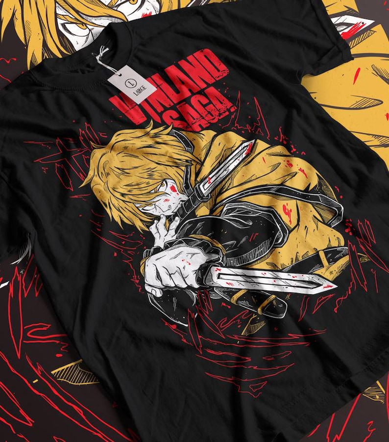 Może przedstawiać: Czarny T-shirt z grafiką blond postaci z anime "Vinland Saga" trzymającej miecz. Postać ma krew na twarzy i ubraniu. Tekst "Vinland Saga" jest napisany czerwonymi literami na koszulce.