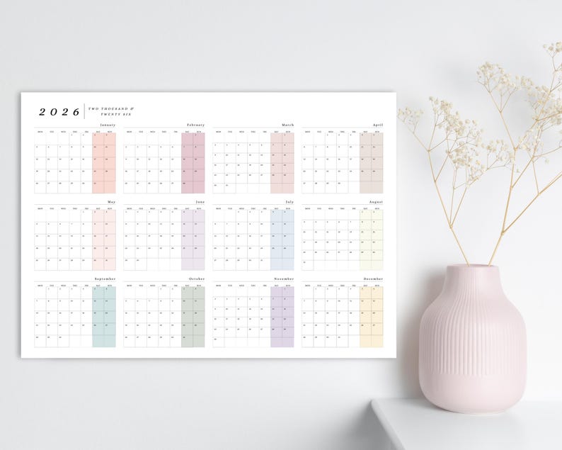 May include: A minimalist 2026 calendar with a white background. Each month is displayed with a pastel color block. A pink vase with white flowers sits to the right.