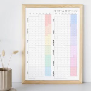 K&ouml;nnte beinhalten: Ein gerahmter Wandkalender mit dem Text "TWENTY & TWENTY SIX" oben. Der Kalender hat ein Rasterlayout mit vertikal aufgelisteten Monaten und horizontalen Daten. Jeder Monat hat einen anderen pastellfarbenen Block.
