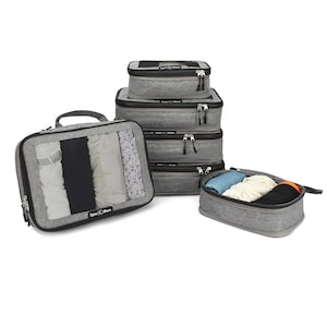 May include: A set of gray packing cubes in various sizes, some with contents visible. One cube has a handle and a mesh front, revealing neatly folded clothing. Other cubes are stacked, and one is open, displaying folded garments.
