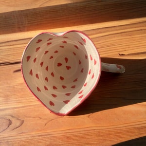 Könnte beinhalten: Eine weiße, herzförmige Schüssel aus Keramik mit rotem Rand und rotem Herzmuster im Inneren.