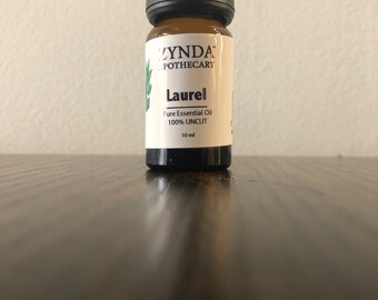 Könnte beinhalten: Eine kleine braune Glasflasche mit schwarzem Verschluss, beschriftet mit "ZYNDA APOTHECARY Laurel Pure Essential Oil 100% UNCUT 10 ml".
