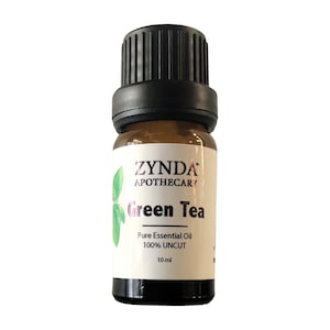 Può includere: Una piccola bottiglia di vetro ambrato con un tappo nero, etichettata "ZYNDA APOTHECARY Green Tea Pure Essential Oil 100% UNCUT 10 ml".