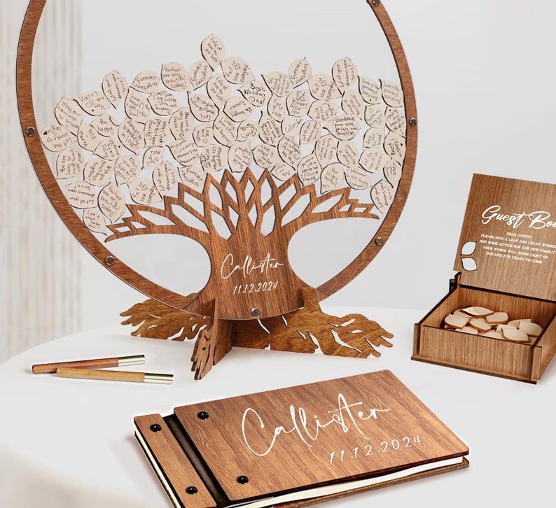 May include: A wooden guest book with a tree design and a clear acrylic circle. The tree has leaves that guests can write on and place in the box. The book is personalized with the name "Callister" and the date "11.12.2024".