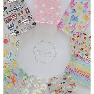 May include: A collection of eight clear phone cases with different colorful patterns. The patterns include hearts, butterflies, bees, dinosaurs, daisies, farm animals, and fire trucks. The cases are all made of clear plastic and have a hole in the center for the phone's camera.