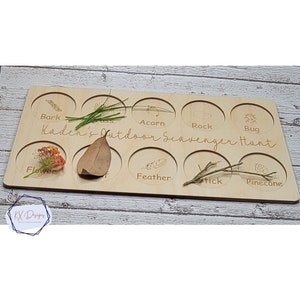 May include: Wooden board with nine circular cutouts, each labeled with a nature item to find on an outdoor scavenger hunt. The labels include: Bark, Grass, Acorn, Rock, Bug, Flower, Leaf, Feather, Stick, and Pinecone. The board is labeled "Kaden's Outdoor Scavenger Hunt".