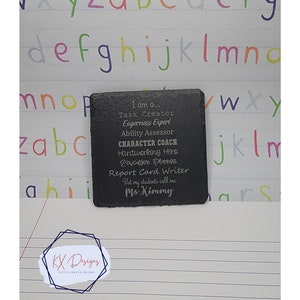 May include: A black slate coaster with an engraved message that reads "I am a... Task Creator, Eagerness Expert, Ability Assessor, CHARACTER COACH, Hardworking Hero, Education Planner, Report Card Writer, But my students call me Ms. Kimmy".