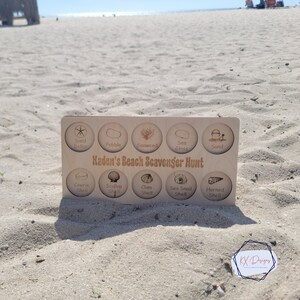 May include: A wooden board with a list of items to find on a beach scavenger hunt. The items include sand dollar, pebble, seaweed, sea glass, sand, cowrie shell, scallop shell, clam shell, sea snail shell, and horned shell. The board is labelled "Kaden's Beach Scavenger Hunt".