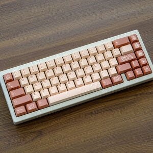 May include: A light beige mechanical keyboard with brown and beige keycaps. The keycaps have various symbols and icons printed on them.