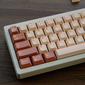 May include: A beige and brown mechanical keyboard with a light beige case and brown keycaps. The keyboard has a standard layout with function keys, number keys, and a space bar. The keycaps have various symbols and letters printed on them.
