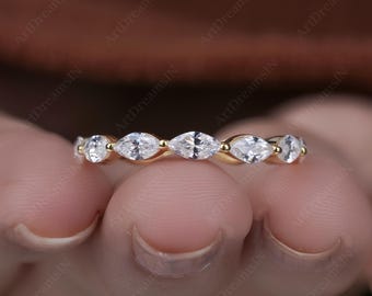 May include: A gold band ring featuring a series of marquise-cut white gemstones. The ring's design showcases a continuous pattern of alternating gemstones, creating a sparkling and elegant aesthetic. The ring is set against a blurred background.