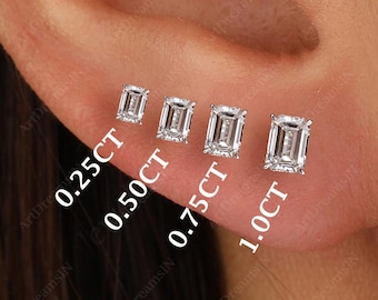 May include: Four emerald cut diamond earrings in different sizes, displayed on a person's earlobe. The earrings are labeled with their carat weight: 0.25CT, 0.50CT, 0.75CT, and 1.0CT.