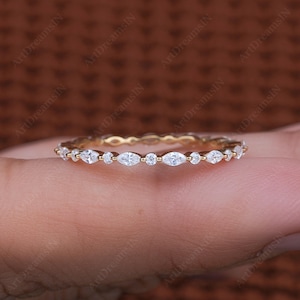 May include: A delicate gold band featuring a row of marquise-shaped diamonds. The diamonds are set in a pave setting and are surrounded by smaller round diamonds.