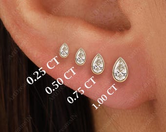 Könnte beinhalten: Vier tropfenförmige Diamant-Ohrringe in verschiedenen Größen, gezeigt am Ohrläppchen einer Person. Die Ohrringe sind mit ihrem Karatgewicht gekennzeichnet: 0,25 CT, 0,50 CT, 0,75 CT und 1,00 CT.