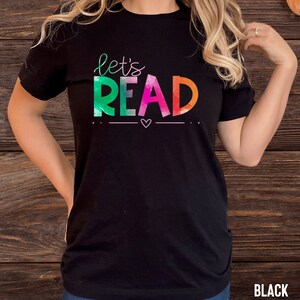 May include: Black t-shirt with the text "let's read" in rainbow colors. The text is stylized with a watercolor effect.