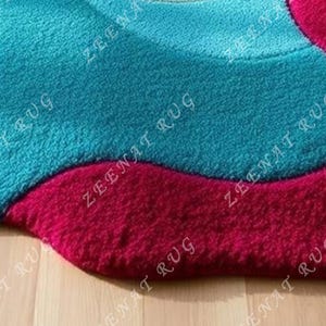 May include: Close-up of a teal blue and burgundy area rug with a wavy design. The rug is made of a soft, plush material.