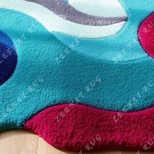 May include: A close-up of a blue and pink abstract area rug with a wavy design. The rug is made of soft, plush material.