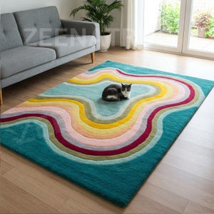 Puede incluir: Una alfombra abstracta colorida con un dise&ntilde;o ondulado en tonos de azul, amarillo, rosa y rojo. Un gato est&aacute; sentado en la alfombra.
