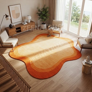 May include: A large, abstract, orange and yellow area rug with a wavy, organic shape. The rug is in a living room with two chairs and a wooden table.