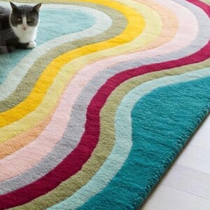 Puede incluir: Una alfombra colorida con un patr&oacute;n ondulado en tonos de azul, verde, amarillo, rosa y rojo. La alfombra est&aacute; hecha de un material suave y mullido.