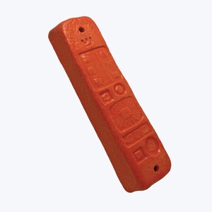 May include: An orange mezuzah case with embossed symbols and a textured surface. The rectangular case has a hole at each end for mounting. The symbols include a sunburst, a Star of David, and Hebrew letters.