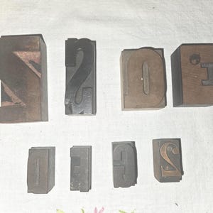 May include: A collection of vintage wooden letterpress printing blocks. The blocks feature the numbers 0, 1, 2, 3, and the letter N. The blocks are made of wood and metal, with a worn, antique appearance.