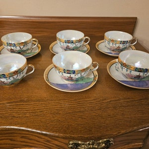 May include: Set of six vintage teacups and saucers with a delicate floral and landscape design. The cups and saucers are white with gold trim and feature a colorful Asian-inspired pattern.
