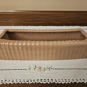 May include: A light brown ceramic planter with a ribbed design. The planter is rectangular and has a wide, shallow opening.