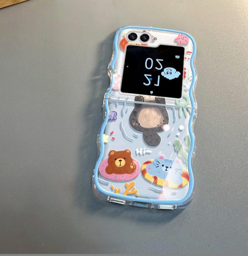 May include: A blue and white phone case with a cartoon bear, cat, and otter design. The case has a small screen on the front that displays the time, 1:50.