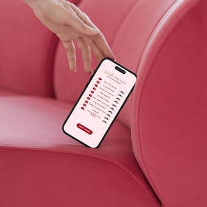 May include: A black smartphone displays a game with red lipstick and mustache icons on a pink background. The phone is held over a pink sofa. The game's title is "Guess the worst finger".