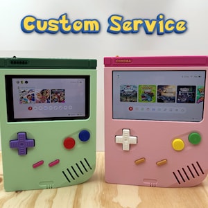 May include: Two handheld gaming consoles with screens displaying game menus. The left console is light green with a dark green top, purple d-pad, red and blue buttons. The right console is pink with a pink top, white d-pad, yellow and green buttons. Text reads Custom Service.